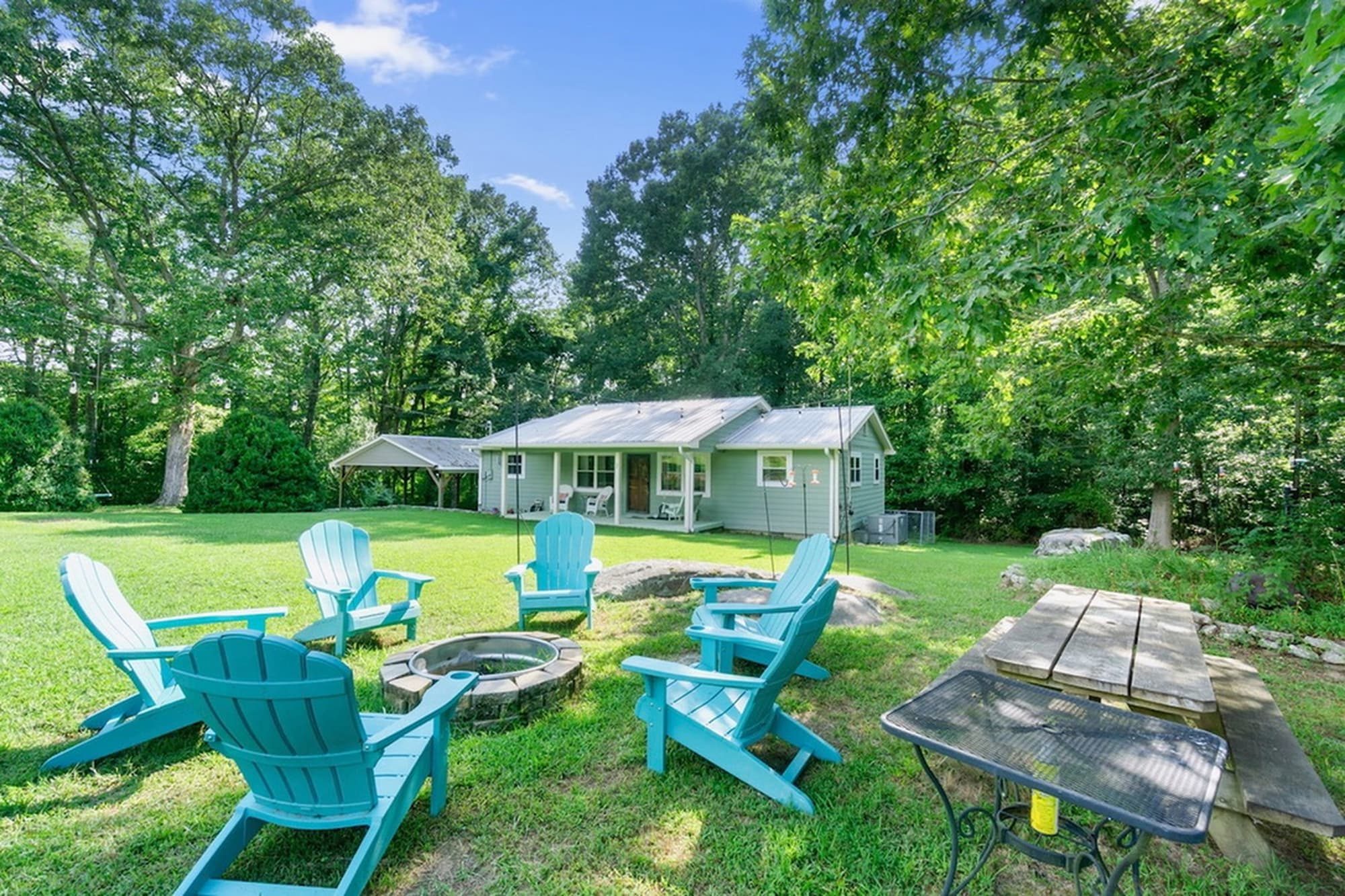 The backyard fire pit circle of teal Adirondack chairs on a summer afternoon