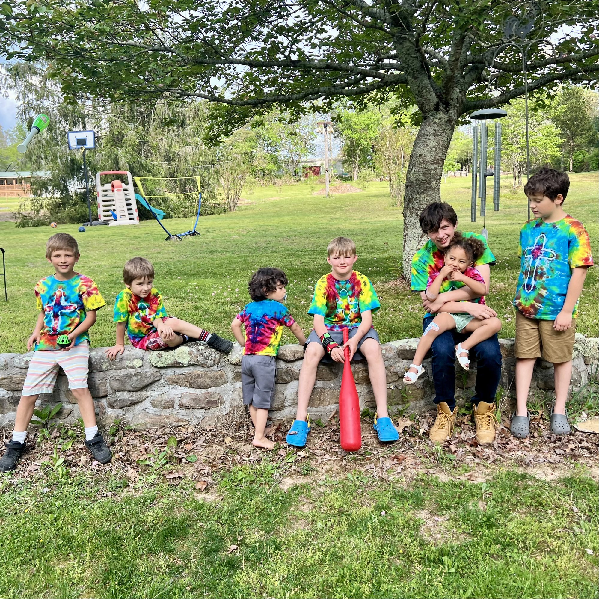 Three generations — all seven grandkids lined up on the stone wall in tie-dye